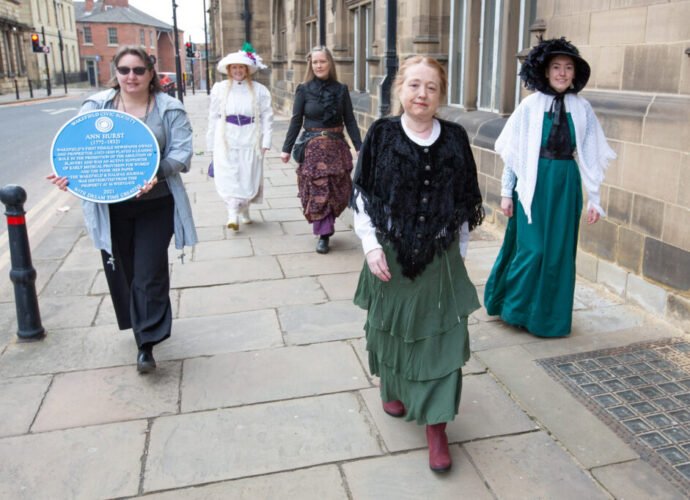 Women in Victorian costume waling down a road in Wakefield with Ann Hurst's Blue Plaque