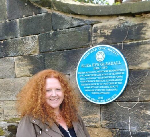 Sarah Cobham stands in front of Eliza Gleadall's Blue Plaque installed on a wall in Heath.