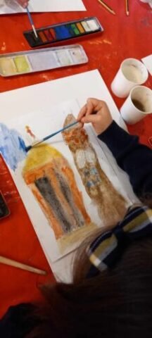 The hand of a child is in frame painting a watercolour picture on a large sheet of paper.