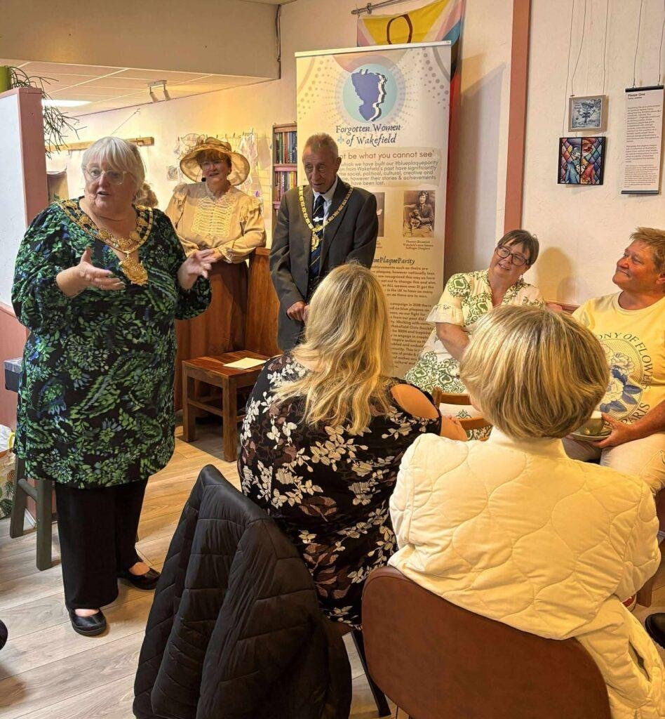 A mayoral figure giving a talk with her consort in the background. 